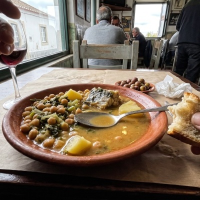Alentejo table in natural light: a bowl of açorda with coriander, a cut loaf of bread and a jug of olive oil