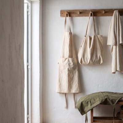 Two off-white bags and t-shirt hanging on wall rack above a bench with clothes and boots.