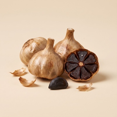 Whole and halved bulbs of black garlic on a beige background