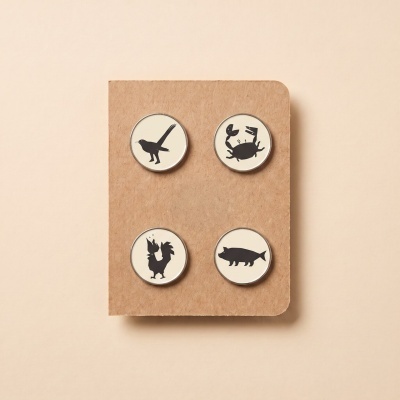 Four round pins with black animals silhouettes on white backgrounds on a brown textured card.