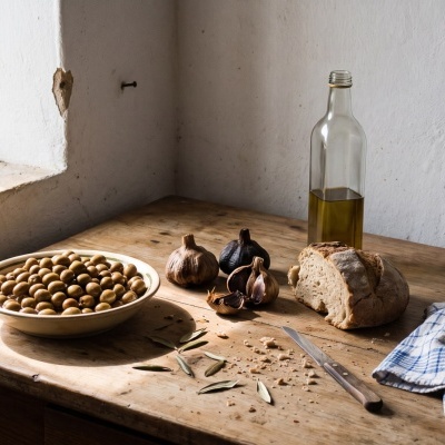 Rustic wooden table with olives, garlic, bread, bottle, knife, cloth, and a cardboard box