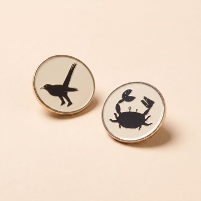 Two round lapel pins with black bird and crab silhouettes