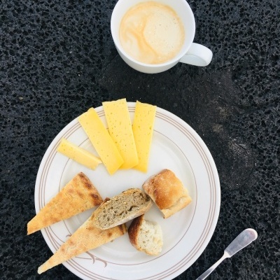 Cup of coffee and plate with cheese slices and bread on black textured surface