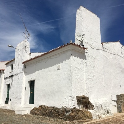 White stucco building with red tile roof and green doors on cobblestone street