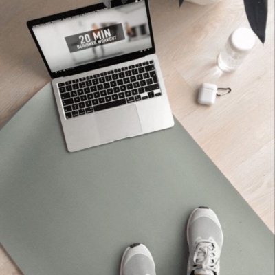 Tapete de exercício cinzento com portátil aberto, garrafa, estojo e sapatos cinzentos