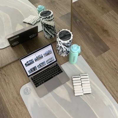 Tapete de yoga cinza claro com rolos de espuma marmoreados, garrafa azul e portátil sobre tapete refletido num espelho