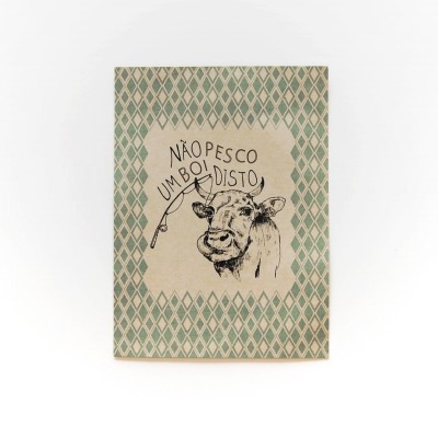 Caderno com capa verde, bege, ilustração de vaca e texto humorístico