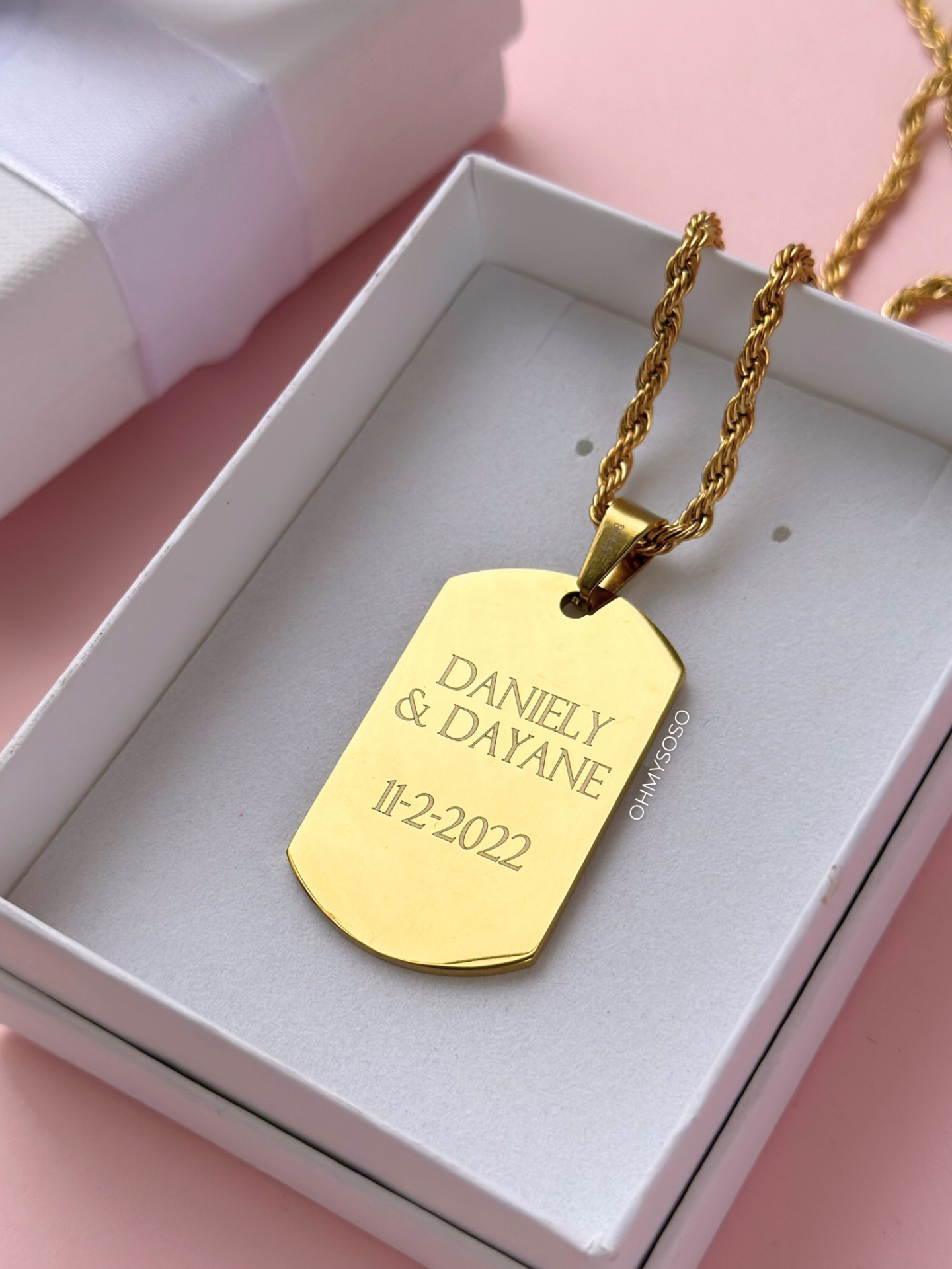 Colar Pai com Foto Colar dourado com pendente gravado em caixa branca sobre fundo rosa