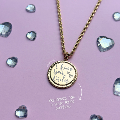 Colar dourado com pendente redondo personalizado com texto em inglês e decoração de corações sobre fundo lilás com corações azuis transparentes