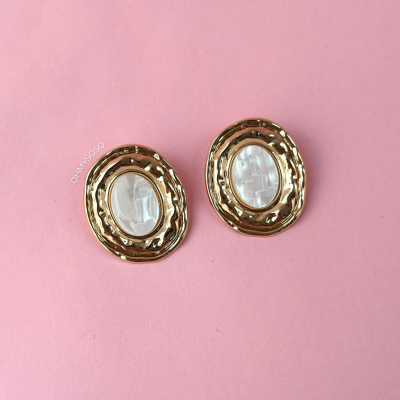 Brincos ovais dourados com pedra translúcida sobre fundo rosa