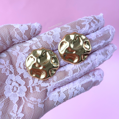 Brincos redondos dourados com textura irregular em mão com luva de renda branca