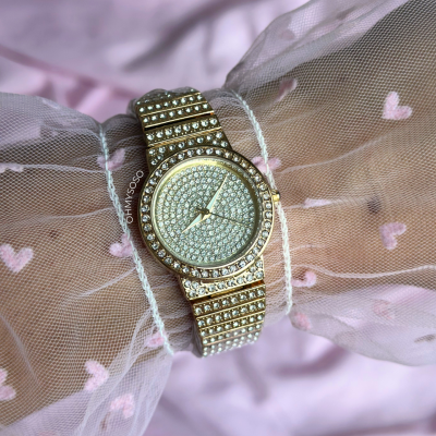 Relógio dourado cravejado de pedras sobre tecido branco com corações cor-de-rosa