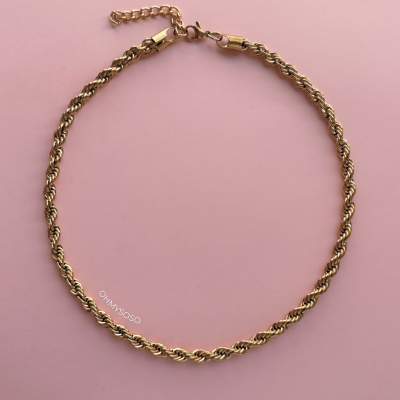 Colar dourado com corrente em espiral sobre fundo rosa claro