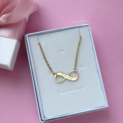 Colar dourado em forma de infinito com data gravada numa caixa de joias branca com laço rosa