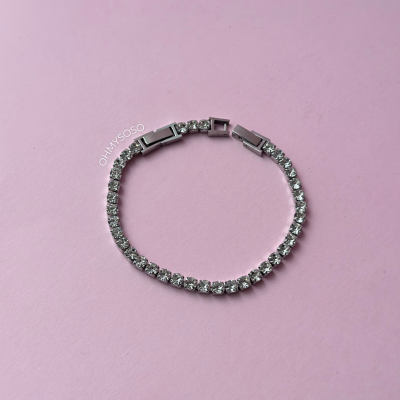 Pulseira tennis com cristais e fecho em metal prateado sobre fundo rosa claro