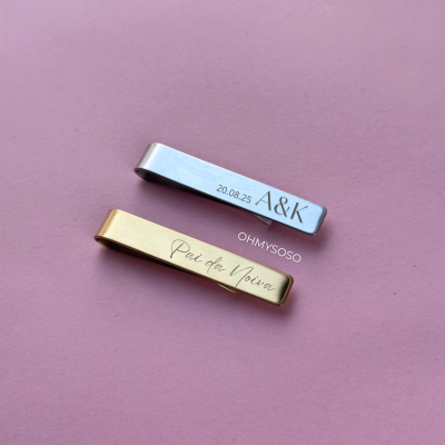 Dois clips para gravata prateado e dourado com inscrições, sobre fundo rosa.