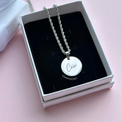 Colar prateado com pendente redondo gravado com o nome Chloé numa caixa branca com interior preto