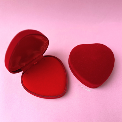 Caixas em formato de coração em veludo vermelho, uma aberta e outra fechada, fundo rosa