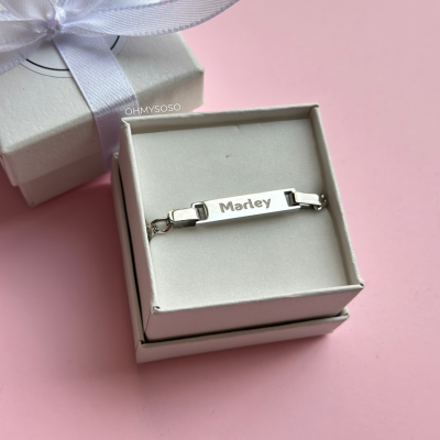 Pulseira prateada com nome num estojo branco sobre fundo rosa