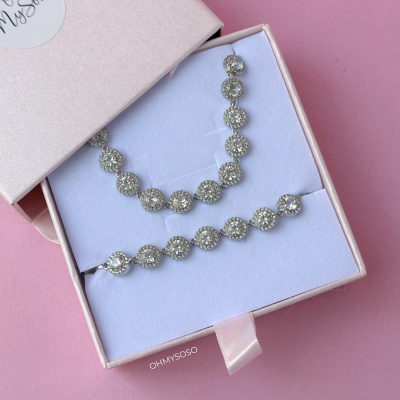 Conjunto de bijuterias prateadas com pedras redondas em caixa rosa claro