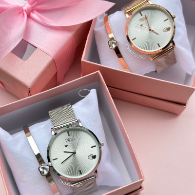Conjuntos de relógios dourado e prateado com pulseiras, em caixas cor-de-rosa com almofadas brancas