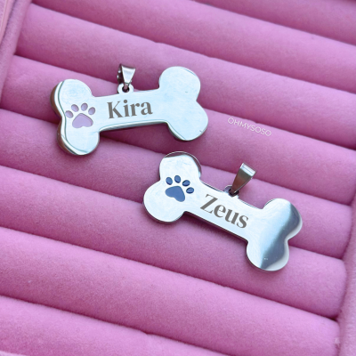 Dois pendentes em forma de osso com nomes e marcas de pata sobre superfície rosa macia