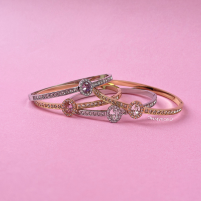 Pulseiras metálicas douradas e prateadas com pedras rosas e pequenos cristais sobre fundo rosa