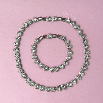 Conjunto de colar e pulseira com pedras em forma de coração em fundo rosa