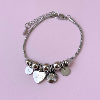 Pulseira prateada com contas e pendentes metálicos sobre fundo rosa