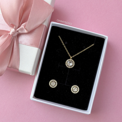 Conjunto de colar e brincos dourados com pedras brilhantes em caixa com fita rosa.