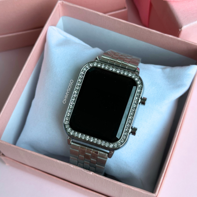 Relógio digital retangular prateado com pedras numa caixa cor-de-rosa