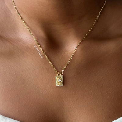 Colar dourado com pendente retangular e diamante central no pescoço