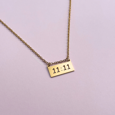 Colar dourado com pendente retangular gravado com o texto 11:11