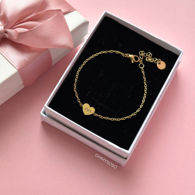 Pulseira dourada com pendente em forma de coração num estojo e caixa com fita rosa