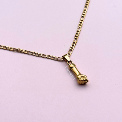 Colar dourado com pendente em forma de punho sobre fundo rosa claro