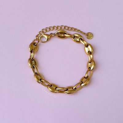 Pulseira dourada com elos ovais sobre fundo rosa.
