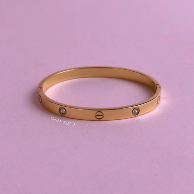 Pulseira rígida dourada com pedras brilhantes e parafusos gravados