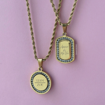 Duas correntes douradas com pendentes gravados e pedras, em fundo rosa