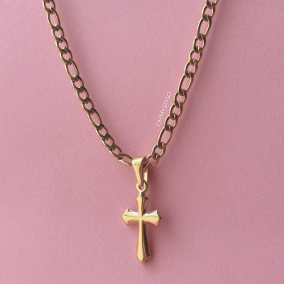 Colar dourado com pendente de cruz sobre fundo rosa