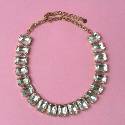 Colar dourado com pedras retangulares transparentes sobre fundo rosa