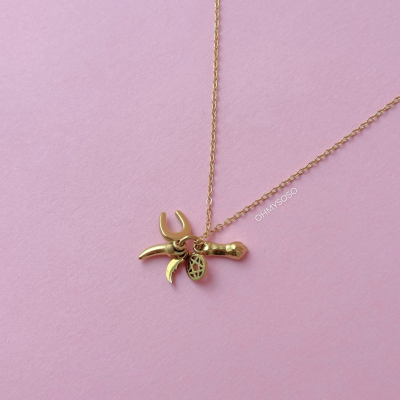 Colar dourado com pendentes variados sobre fundo rosa claro