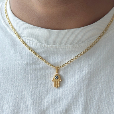 Colar dourado com pendente de mão e olho, sobre t-shirt branca.