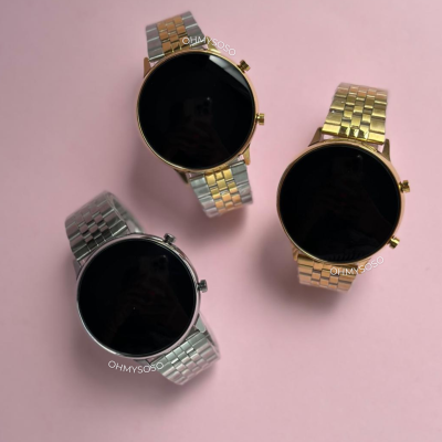 Três relógios de mostrador preto com braceletes metálicas prateada, dourada e bicolor em fundo rosa.