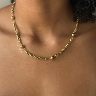 Colar dourado com correntes e bolas espaçadas no pescoço.