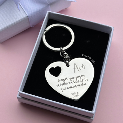 Chaveiro em forma de coração prateado numa caixa preta com tampa cinza e fita azul