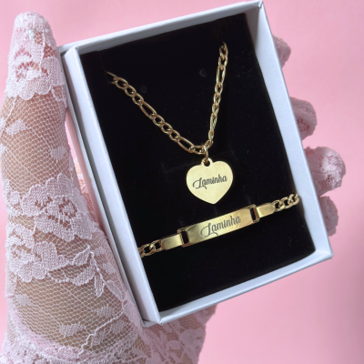 Conjunto de joalharia dourada com pulseira e colar gravados com a palavra Laminha, apresentados em caixa preta e branca