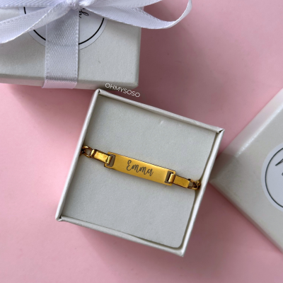 Pulseira dourada com inscrição Emma em caixa branca sobre fundo rosa