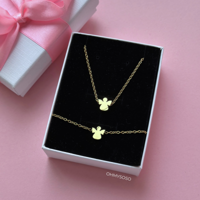 Conjunto de colar e pulseira dourados com pendentes de anjos numa caixa branca com interior preto, ao lado caixa branca com fita rosa.