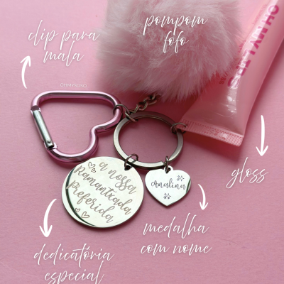 Porta-chaves com dip em forma de coração, pompom rosa, medalhas com gravação e gloss sobre fundo rosa.