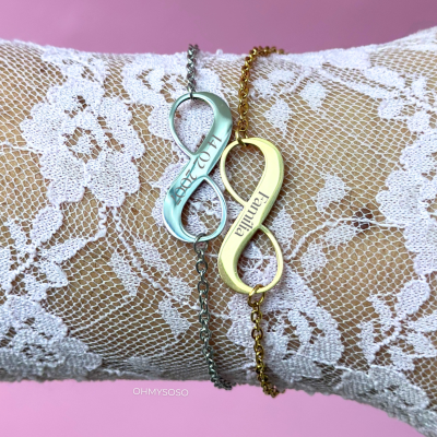 Dois colares com pendentes em forma de infinito, prata e dourado, com textos gravados e fundo rosa.